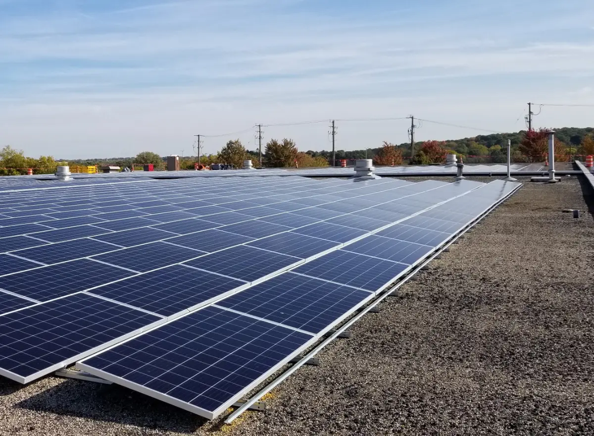 A large array of solar panels installed on a flat, gravel-covered rooftop under a clear blue sky.