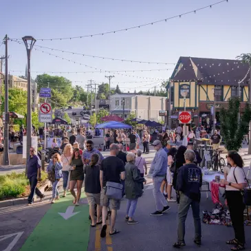 People gather on a street lined with shops and food vendors during an outdoor market event.