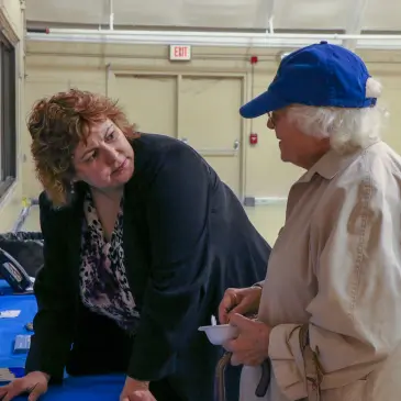 A woman in a suit and a woman in a blue cap converse at a table with health resources.