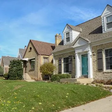 Row of well-maintained single-family homes with manicured lawns and blue sky.