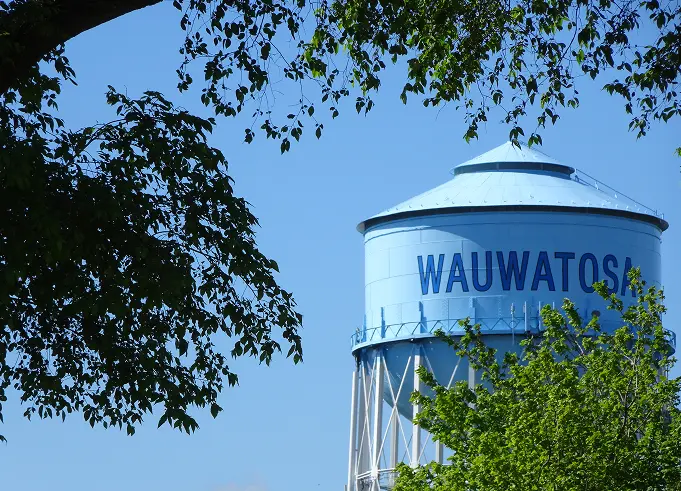A light blue water tower with "WAUWATOSA" written in dark blue letters against a clear blue sky.
