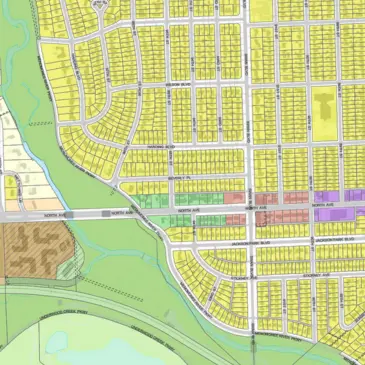 Aerial view of a city zoning map showing residential blocks, streets, and green spaces with different colored zones.