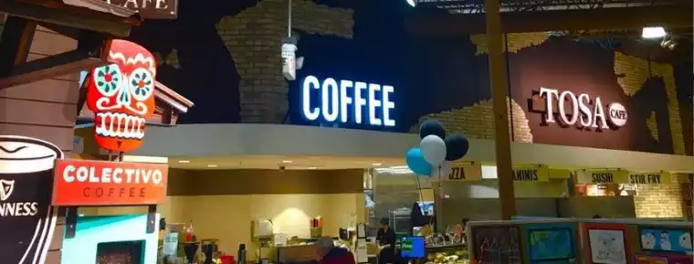 A brightly lit coffee shop with signs for COLECTIVO COFFEE, COFFEE, and TOSA CAFE. A colorful skull decoration is visible.