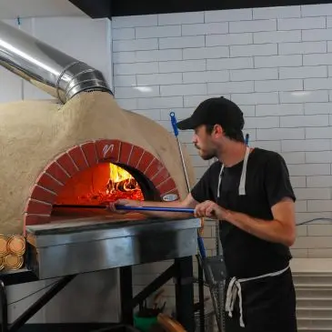 Chef uses a pizza peel to place a pizza into a wood-fired oven.