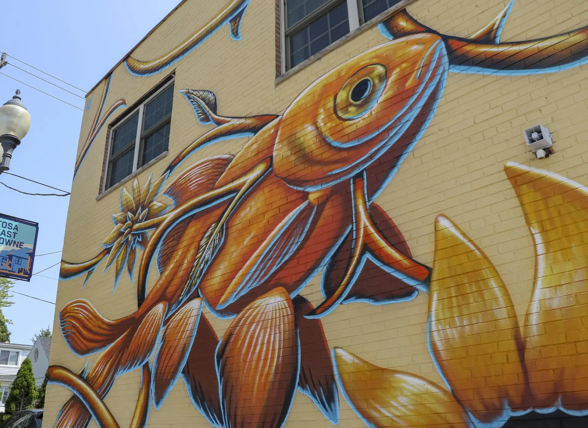 A vibrant mural of an orange fish with blue outlines on a yellow brick building.