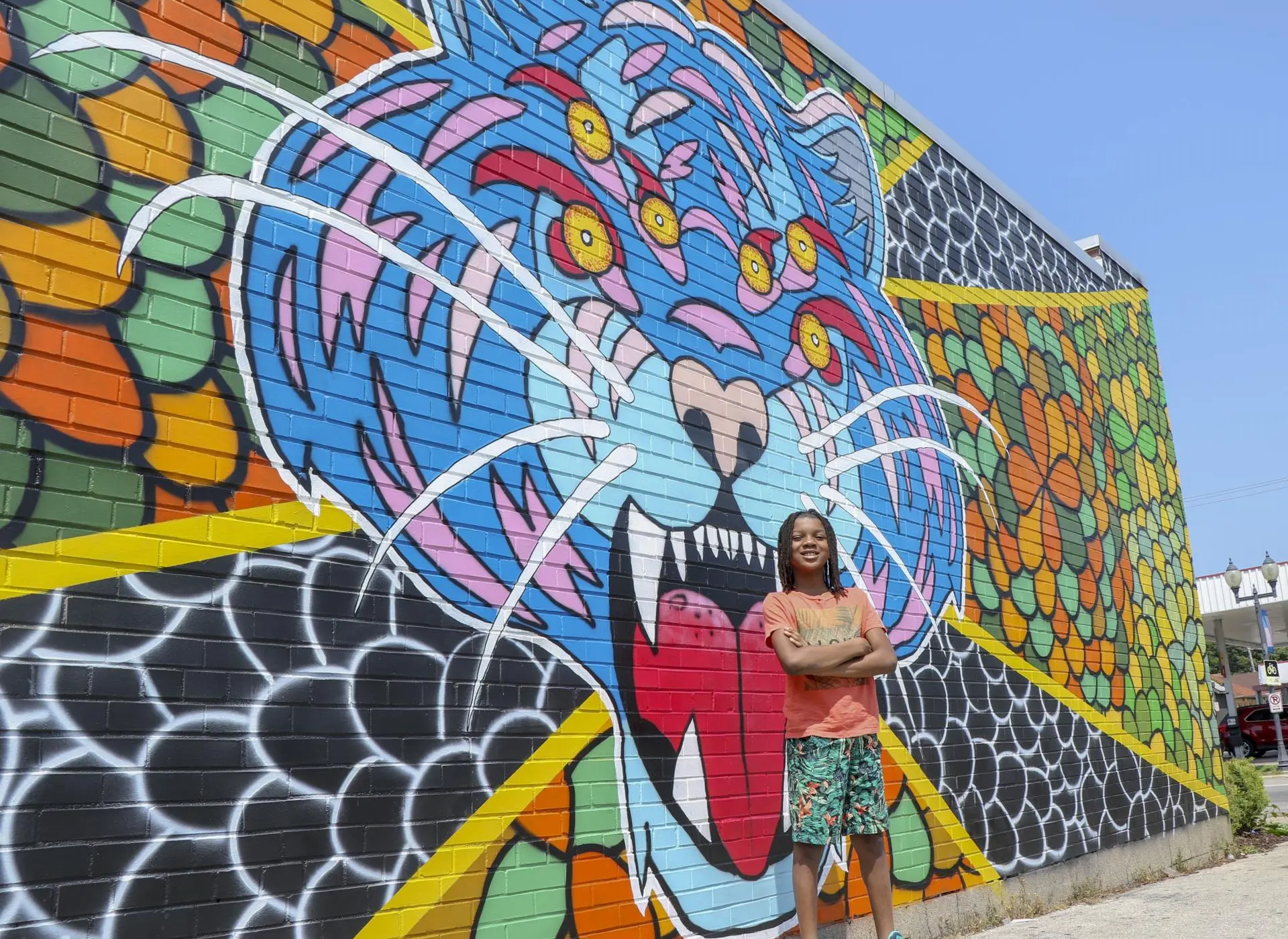 A young person stands in front of a vibrant mural of a blue tiger's face on a brick wall.