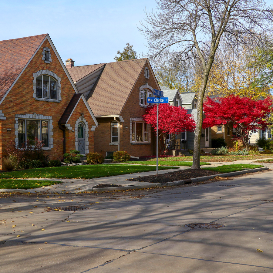 Brick houses line a street with a "68 Clarke St" street sign and vibrant red trees in autumn.