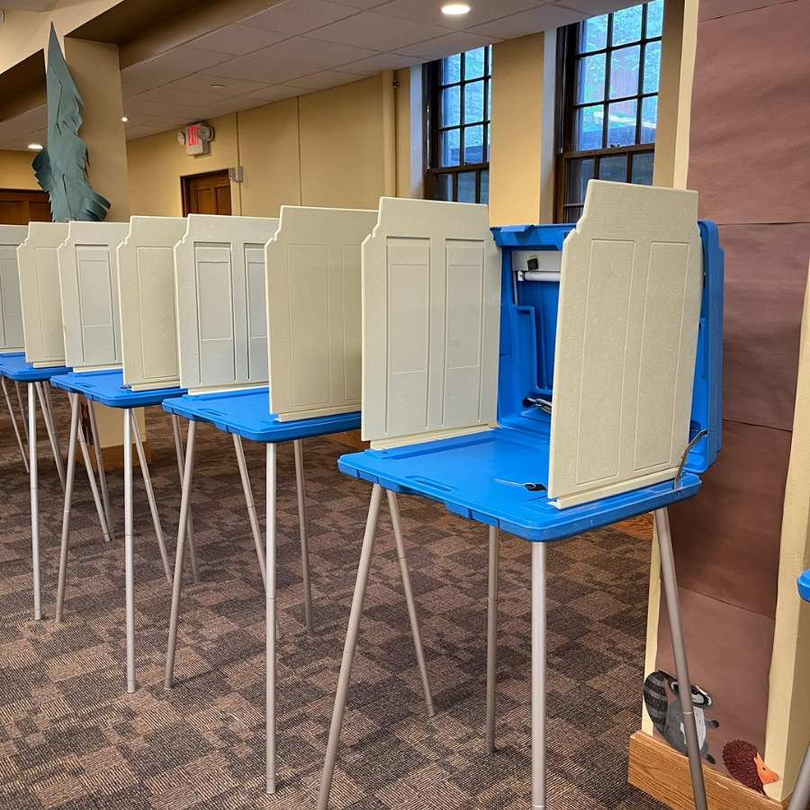 A row of blue and beige voting booths with privacy screens stand on a patterned carpet.