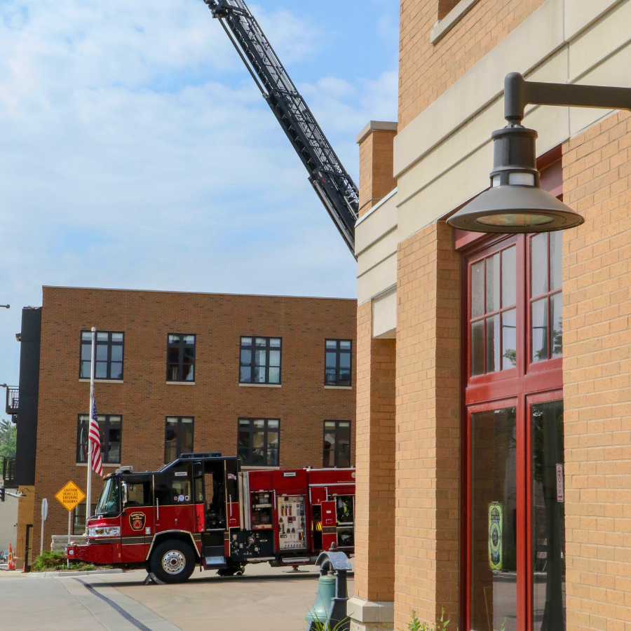 A red fire truck with an extended ladder is parked outside a brick building with large windows.