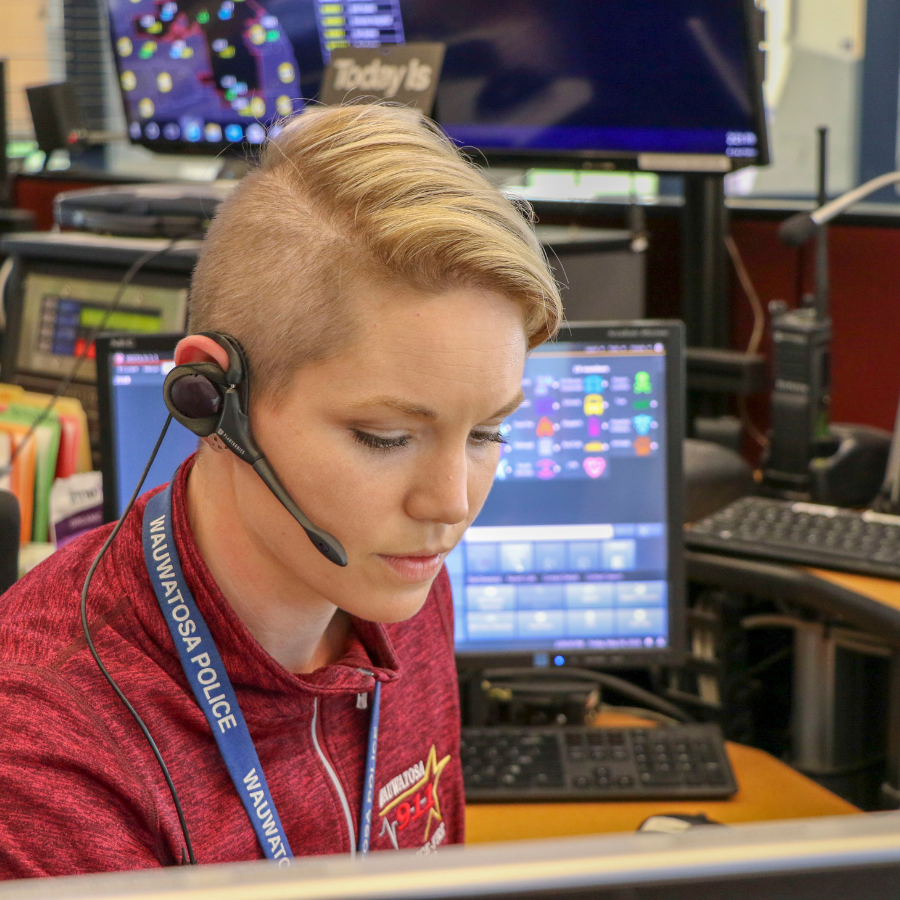 Wauwatosa Police dispatcher wearing a headset and maroon uniform, looking at computer screens.